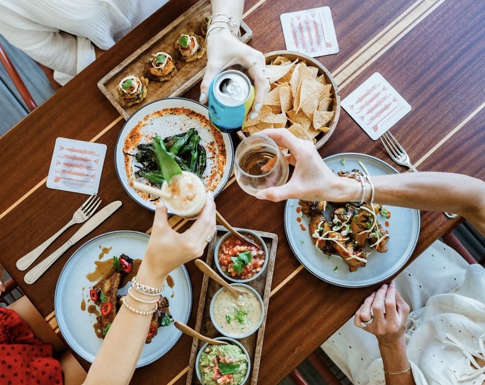 Overhead view of a local Caribbean dining spread with small plates, dips, and guests toasting
