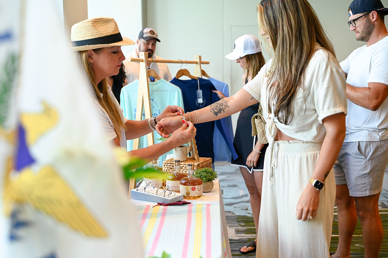 Host helping a guest select a bracelet at a curated gifting station with branded apparel and local rum